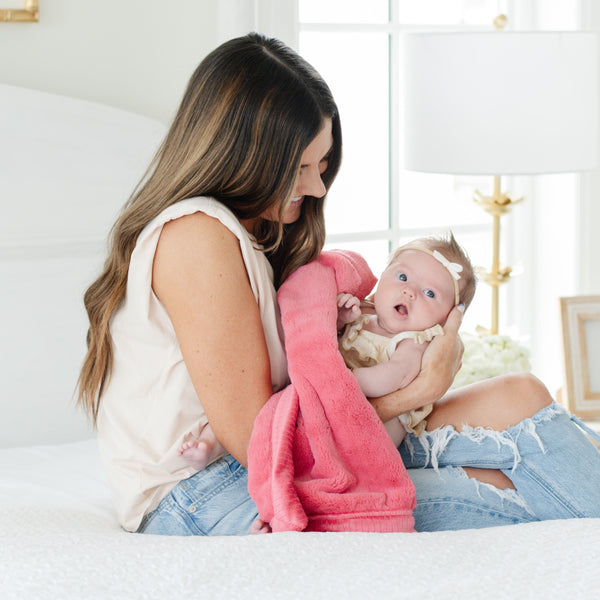 A mother holds her baby girl in a Mini Primrose (bold pink) Colored Lush Saranoni Blanket. The soft blanket is a small blanket and a baby blanket or toddler blanket.