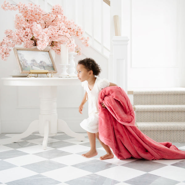 A little girl holds a Toddler Primrose (bold pink) Colored Lush Luxury Saranoni Blanket. The soft blanket is a baby blanket or toddler blanket.