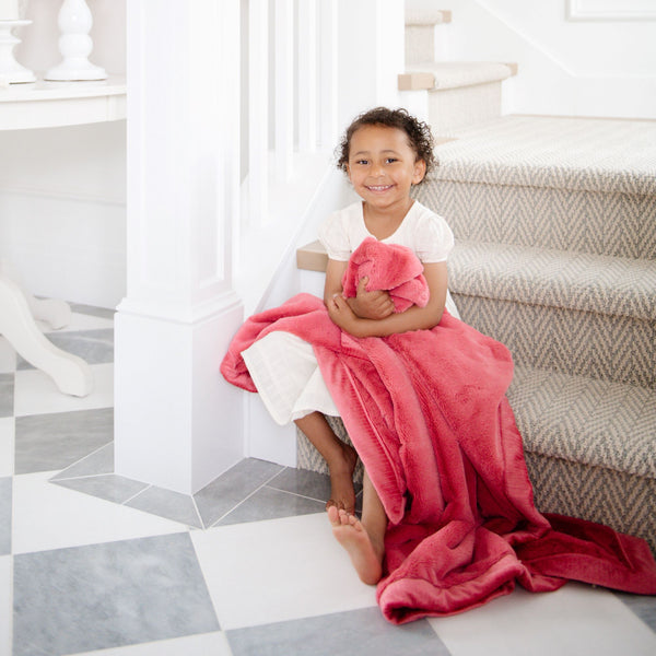 A little girl holds a Toddler Primrose (bold pink) Colored Lush Luxury Saranoni Blanket. The soft blanket is a baby blanket or toddler blanket.