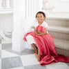 A little girl holds a Toddler Primrose (bold pink) Colored Lush Luxury Saranoni Blanket. The soft blanket is a baby blanket or toddler blanket.