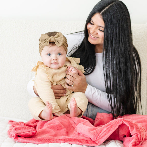 A mother holds her baby girl on a Primrose (bold pink) Colored Lush Saranoni Blanket. The soft blanket is a small blanket and a baby blanket or toddler blanket.