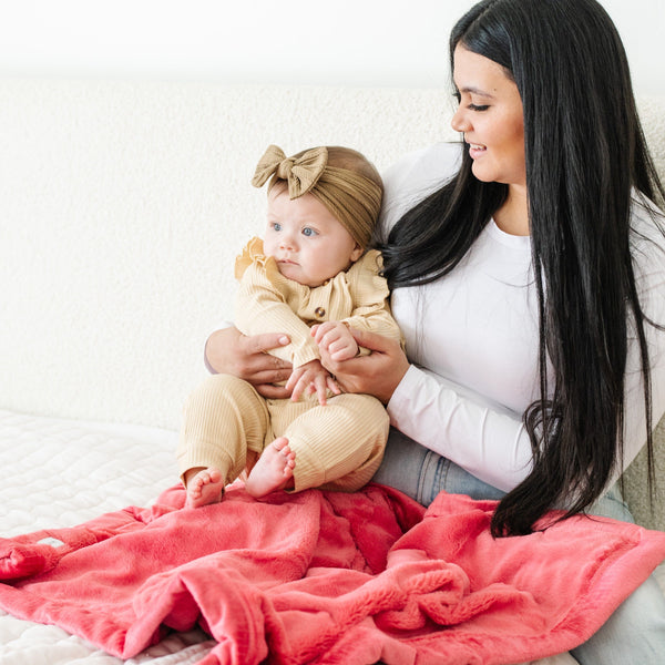 A mother holds her baby girl on a Primrose (bold pink) Colored Lush Saranoni Blanket. The soft blanket is a small blanket and a baby blanket or toddler blanket.