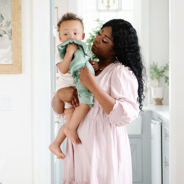 A mother holds her baby boy in a Mini Seagrass (dusty green) Colored Lush Saranoni Blanket. The soft blanket is a small blanket and a baby blanket or toddler blanket.