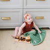 A baby girl holds a Mini Seagrass (dusty green) Colored Lush Saranoni Blanket. The soft blanket is a small blanket and a baby blanket or toddler blanket.