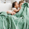 A little girl and her two brothers sit holding a Toddler Seagrass (dusty green) Colored Lush Luxury Saranoni Blanket. The soft blanket is a baby blanket or toddler blanket.