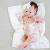 Baby laying with a cozy ivory satin border mini blanket. 