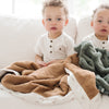 Two young boys sitting on the couch snuggling with their favorite caramel and green satin border blankets.