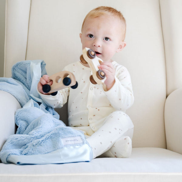 Little boy playing while snuggled up with a light blue satin border blanket.