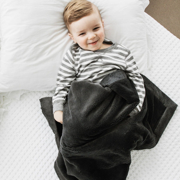 A little boy lays under a Luxury Receiving Charcoal Colored Lush Saranoni Blanket. The soft blanket is a small blanket and a baby blanket or toddler blanket.