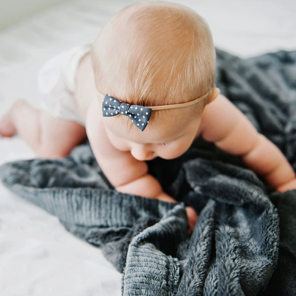 A baby girl crawls on top of a Charcoal Colored Lush Saranoni Blanket. The soft blanket is a small blanket and a baby blanket.