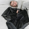 A little boy lays on a Luxury Receiving Charcoal Colored Lush Saranoni Blanket. The soft blanket is a small blanket and a baby blanket or toddler blanket.