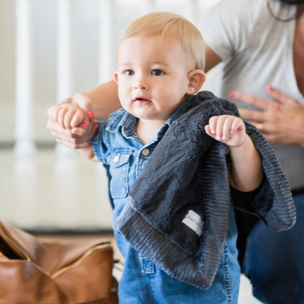 A baby boy walks with a Charcoal Colored Lush Saranoni Blanket. The soft blanket is a small blanket and a baby blanket or toddler blanket.