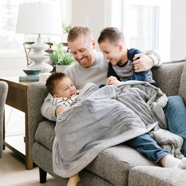 Two little boys who are brothers and their Dad sit under a Luxury Toddler Gray Colored Lush Saranoni Blanket. The soft blanket is a toddler blanket or baby blanket.