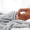 A woman lays under a Luxury Extra Large Oversized Throw Gray Colored Lush Saranoni Blanket. The soft blanket is an extra large throw blanket and has a soft faux fur feeling.