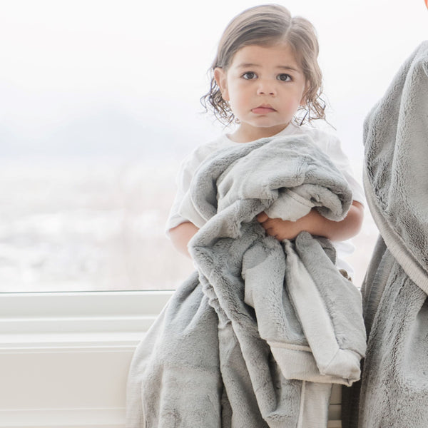 A little girl holds a Luxury Receiving Gray Colored Lush Saranoni Blanket. The soft blanket is a small blanket and a baby blanket or toddler blanket.