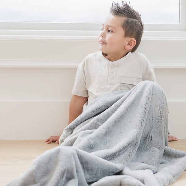 A little boy sits under a Luxury Toddler Gray Colored Lush Saranoni Blanket. The soft blanket is a toddler blanket or baby blanket.