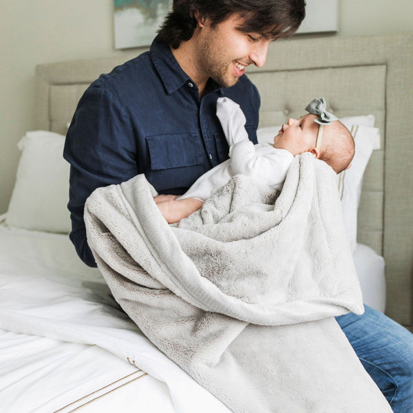 A father holds his baby girl in a Luxury Receiving Feather (light gray) Colored Lush Saranoni Blanket. The soft blanket is a small blanket and a baby blanket or toddler blanket.