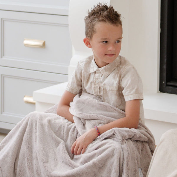 A boys holds a Luxury Toddler Feather (light gray) Colored Lush Saranoni Blanket. The soft blanket is a baby blanket or toddler blanket.