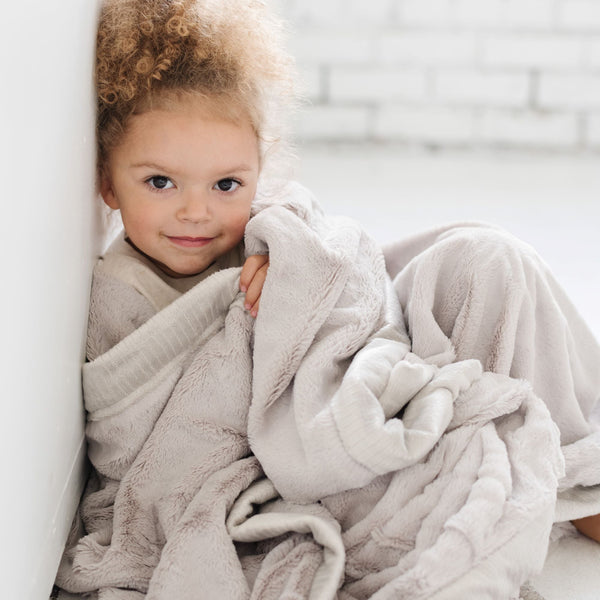 A little girl is wrapped in a Luxury Toddler Feather (light gray) Colored Lush Saranoni Blanket. The soft blanket is a baby blanket or toddler blanket.