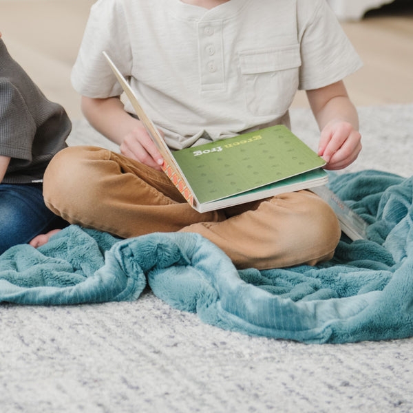 A little boy sits on a Mineral Blue Colored Lush Saranoni Blanket. The soft blanket is a small blanket and a baby blanket or toddler blanket.