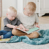 A two little boys sit on a Luxury Receiving Mineral Blue Colored Lush Saranoni Blanket. The soft blanket is a small blanket and a baby blanket or toddler blanket.