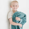 A little boy holds a Toddler Mineral Blue Colored Lush Luxury Saranoni Blanket. The soft blanket is a small blanket and a baby blanket or toddler blanket.