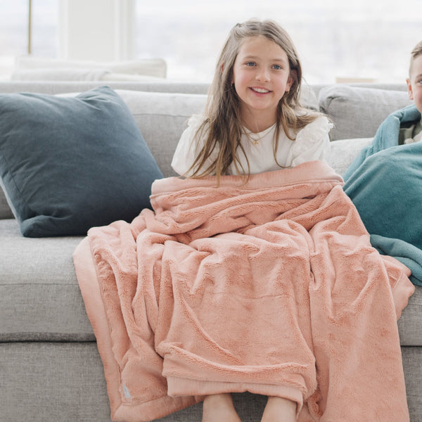 A little girl holds a Toddler Blossom (light peachy pink) Colored Lush Luxury Saranoni Blanket. The soft blanket is a small blanket and a baby blanket or toddler blanket.