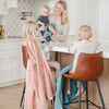 A little girl holds a Toddler Blossom (light peachy pink) Colored Lush Luxury Saranoni Blanket. The soft blanket is a small blanket and a baby blanket or toddler blanket. Her mother and two brothers are by her with Mineral Blue Lush Saranoni Blankets.