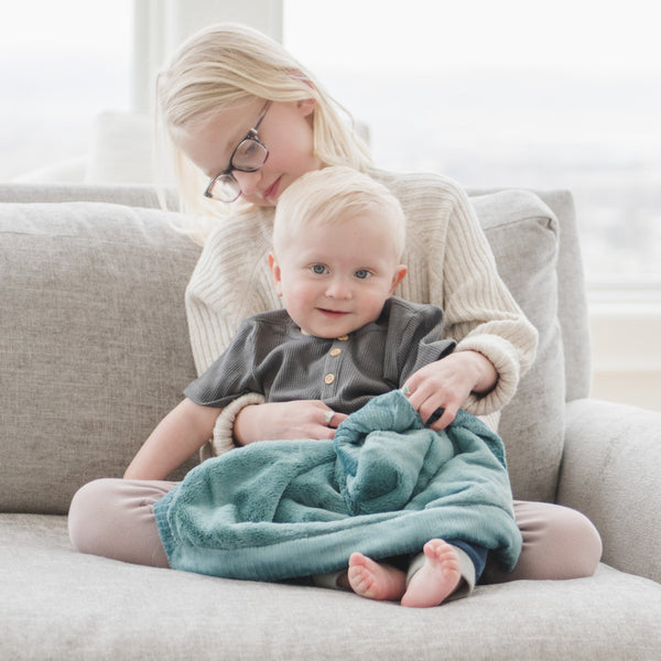 A little boy holds a Mini Mineral Blue Colored Lush Saranoni Blanket. The soft blanket is a small blanket and a baby blanket or toddler blanket.