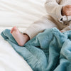 A baby boy sits on a Mini Mineral Blue Colored Lush Saranoni Blanket. The soft blanket is a small blanket and a baby blanket or toddler blanket.