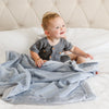 A little boy sits under a Luxury Receiving Storm Cloud (dusty blue gray) Colored Lush Saranoni Blanket. The soft blanket is a small blanket and a baby blanket or toddler blanket.