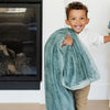 A little boy carries a Luxury Toddler Eucalyptus Colored Lush Saranoni Blanket. The soft blanket is a toddler blanket or baby blanket.