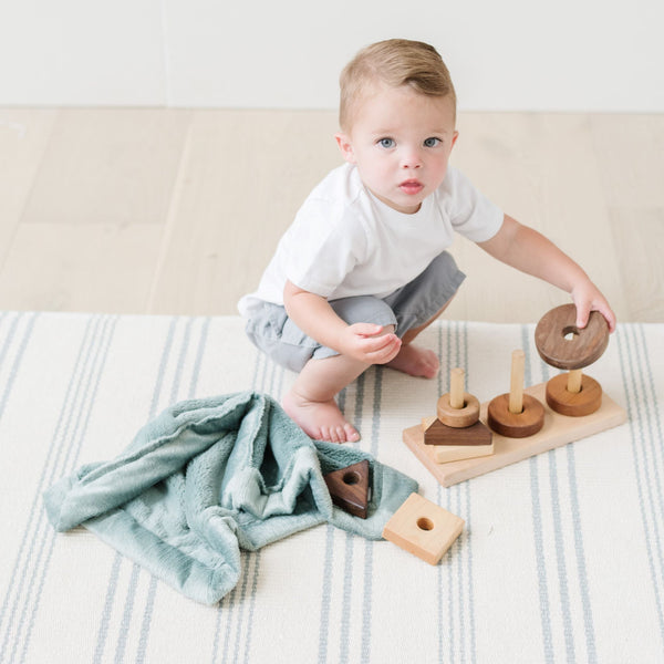 A little boy plays with toys by a Eucalyptus Colored Lush Saranoni Blanket. The soft blanket is a small blanket and a baby blanket.