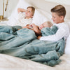 Three brothers sit while holding a Luxury Extra Large Oversized Throw Eucalyptus Colored Lush Saranoni Blanket. The soft blanket is an extra large throw blanket and has a soft faux fur feeling.