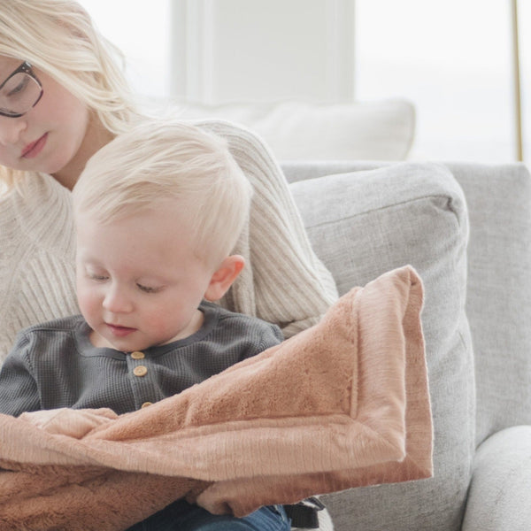 A little boy holds a mini Rosy (dusty peach) Colored Lush Saranoni Blanket. The soft blanket is a small blanket and a baby blanket or toddler blanket.