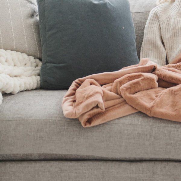 A Luxury Receiving Rosy (dusty peach) Colored Lush Saranoni Blanket on a couch. The soft blanket is a small blanket and a baby blanket or toddler blanket.