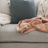 A Luxury Receiving Rosy (dusty peach) Colored Lush Saranoni Blanket on a couch. The soft blanket is a small blanket and a baby blanket or toddler blanket.