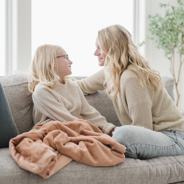 A little girl sits under a Luxury Receiving Rosy (dusty peach) Colored Lush Saranoni Blanket by her Mom. The soft blanket is a small blanket and a baby blanket or toddler blanket.