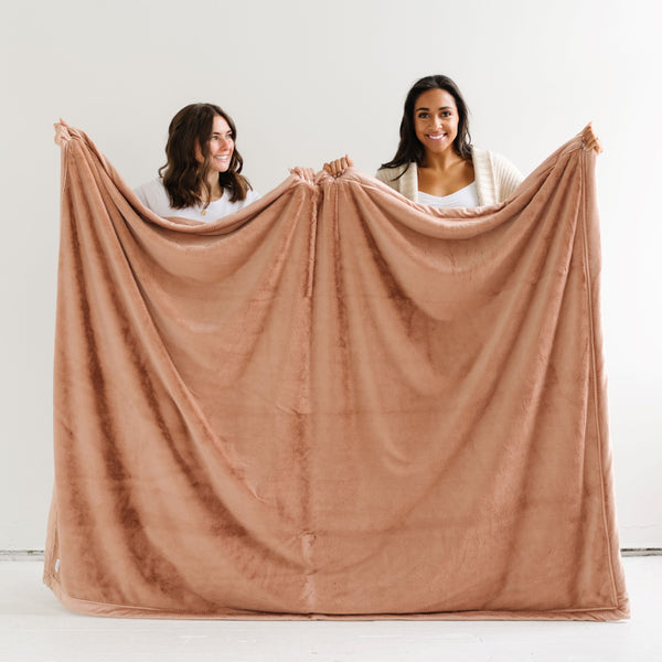 Two girls hold a Luxury Extra Large Oversized Throw Rosy (dusty peach) Colored Lush Saranoni Blanket. The soft blanket is an extra large throw blanket and has a soft faux fur feeling.