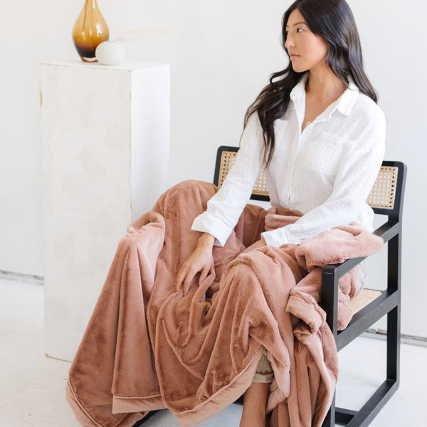 A woman holds a Luxury Extra Large Oversized Throw Rosy (dusty peach) Colored Lush Saranoni Blanket. The soft blanket is an extra large throw blanket and has a soft faux fur feeling.