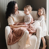 A mother and her child sit under a Luxury Receiving Rosy (dusty peach) Colored Lush Saranoni Blanket. The soft blanket is a small blanket and a baby blanket or toddler blanket.