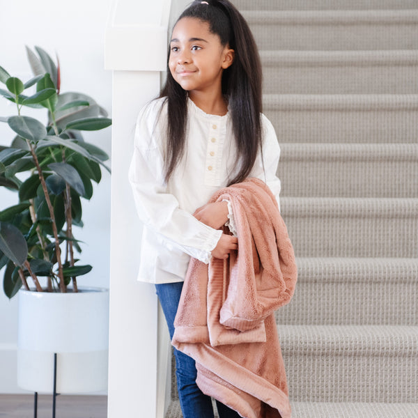 A little girl holds a Toddler Rosy (dusty peach) Colored Lush Luxury Saranoni Blanket. The soft blanket is a small blanket and a baby blanket or toddler blanket.