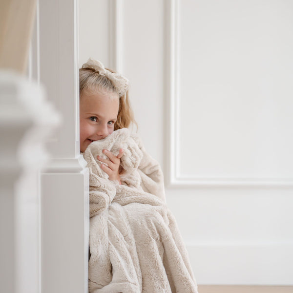 A little girl holds a Luxury Receiving Buttermilk (light tan) Colored Lush Saranoni Blanket. The soft blanket is a small blanket and a baby blanket or toddler blanket.