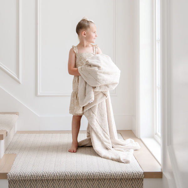 A little girl holds a Toddler Buttermilk (light tan) Colored Lush Luxury Saranoni Blanket. The soft blanket is a small blanket and a baby blanket or toddler blanket.