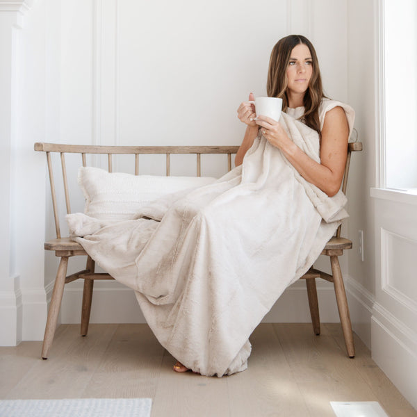 A woman holds a Luxury Extra Large Oversized Throw Buttermilk (light tan) Colored Lush Saranoni Blanket. The soft blanket is an extra large throw blanket and has a soft faux fur feeling.