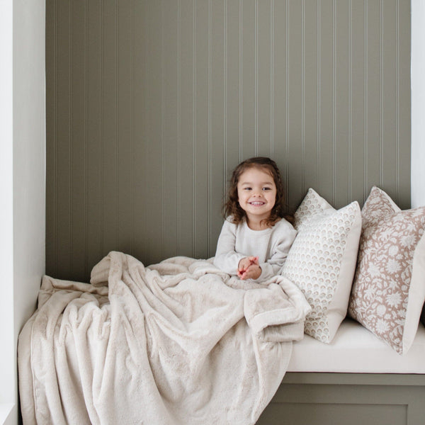 A little girl holds a Toddler Buttermilk (light tan) Colored Lush Luxury Saranoni Blanket. The soft blanket is a small blanket and a baby blanket or toddler blanket.