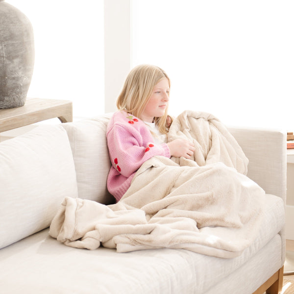 A little girl holds a Toddler Buttermilk (light tan) Colored Lush Luxury Saranoni Blanket. The soft blanket is a small blanket and a baby blanket or toddler blanket.