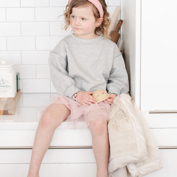 A little girl holds a Luxury Receiving Buttermilk (light tan) Colored Lush Saranoni Blanket. The soft blanket is a small blanket and a baby blanket or toddler blanket.