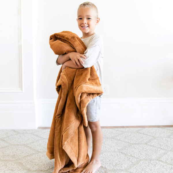 A little boy holds a Luxury Toddler Camel (light yellowish brown) Colored Lush Saranoni Blanket. The soft blanket is a toddler blanket or baby blanket.