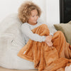 A little girl sits under a Luxury Toddler Camel (light yellowish brown) Colored Lush Saranoni Blanket. The soft blanket is a toddler blanket or baby blanket.